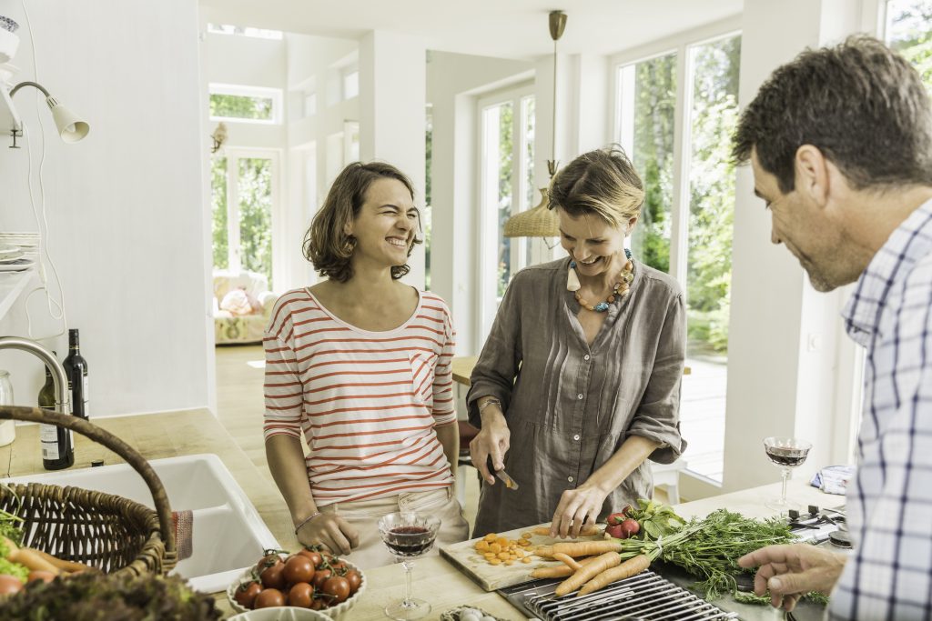 Three adults chatting whilst preparing fresh vegetables in kitchen